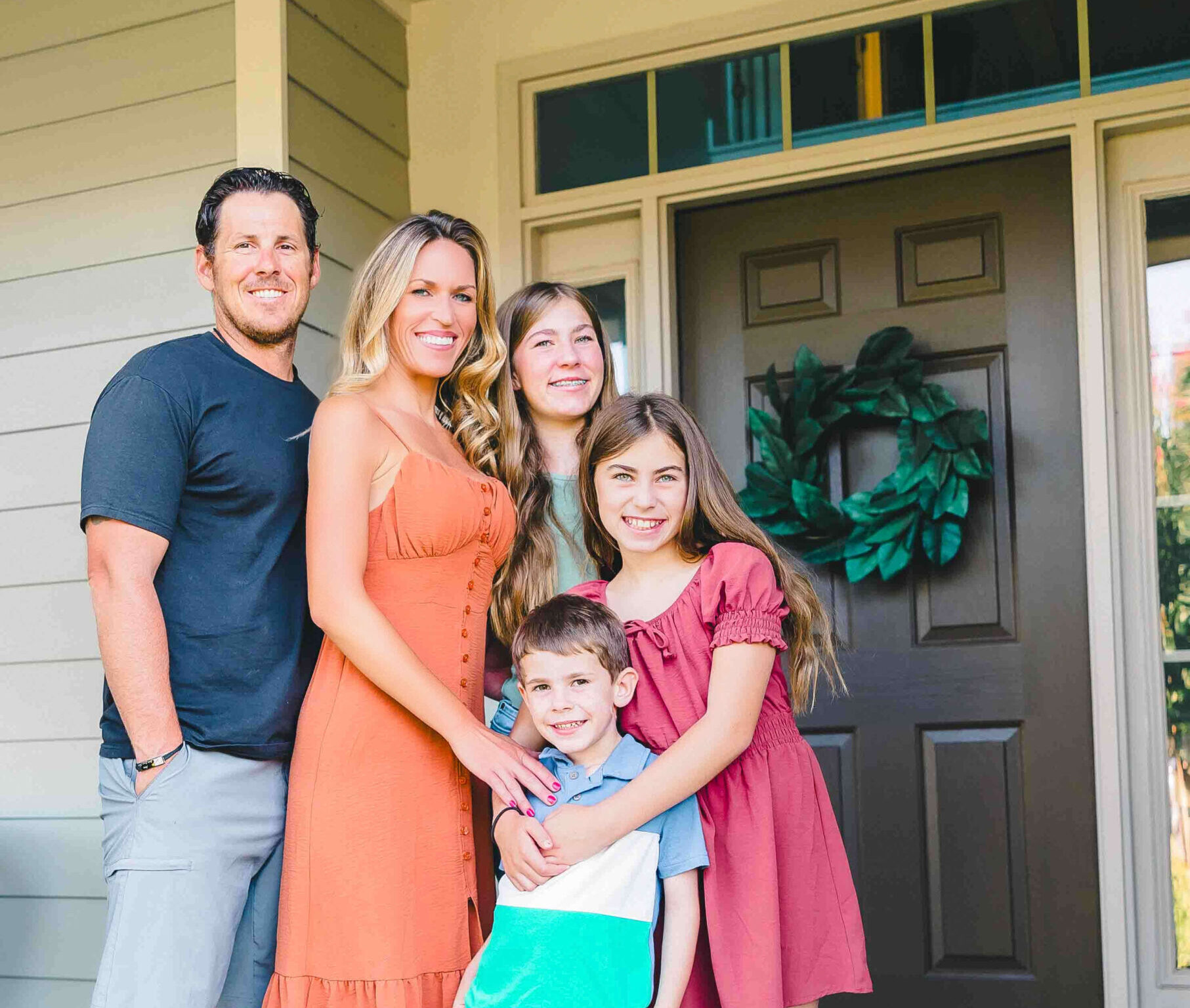 A happy family of 5 hug and smile while standing on a porch before visiting birthday party venues for kids