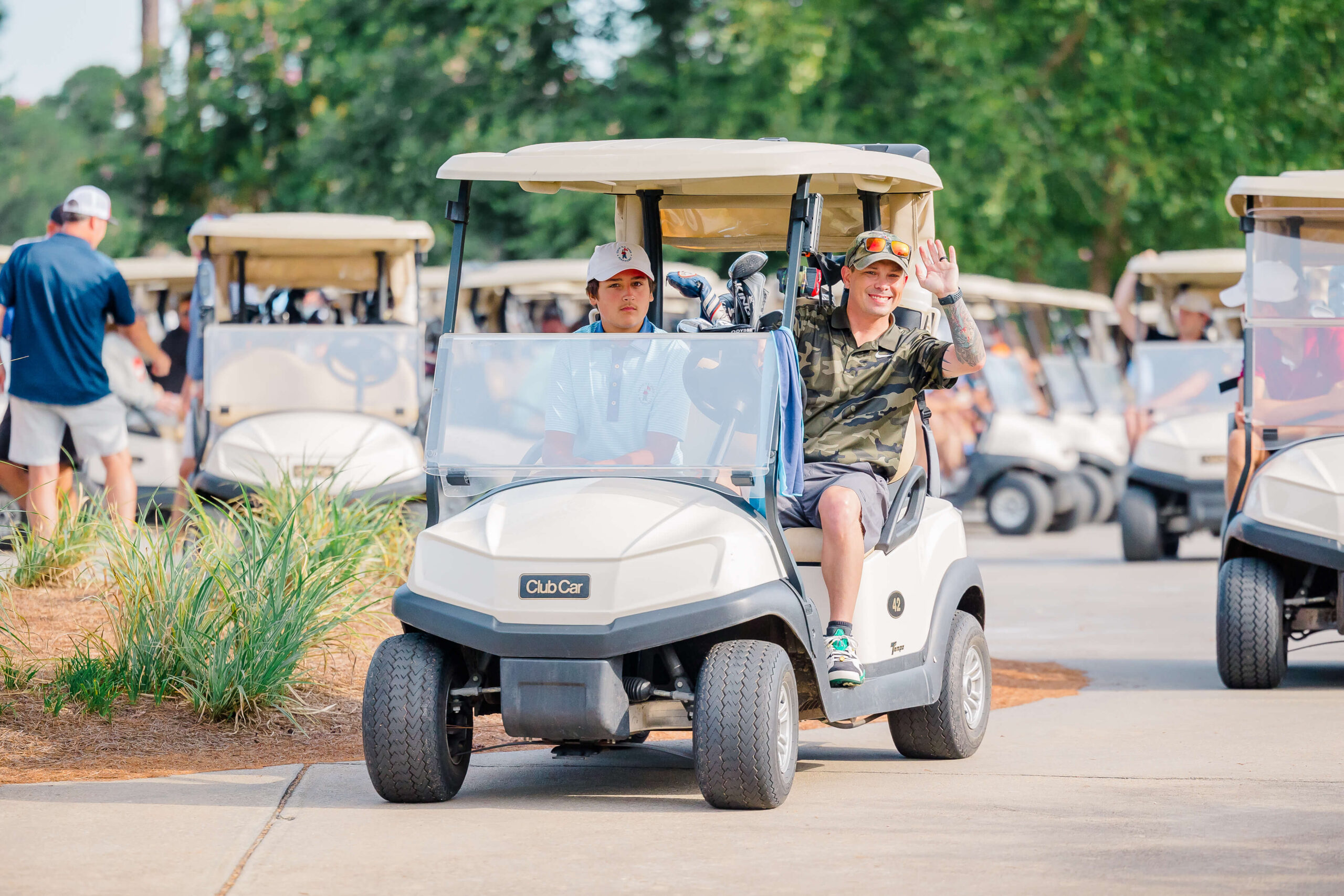 Two men drive a golf cart while one waves with several other golf carts after some mini golf in Fayetteville nc