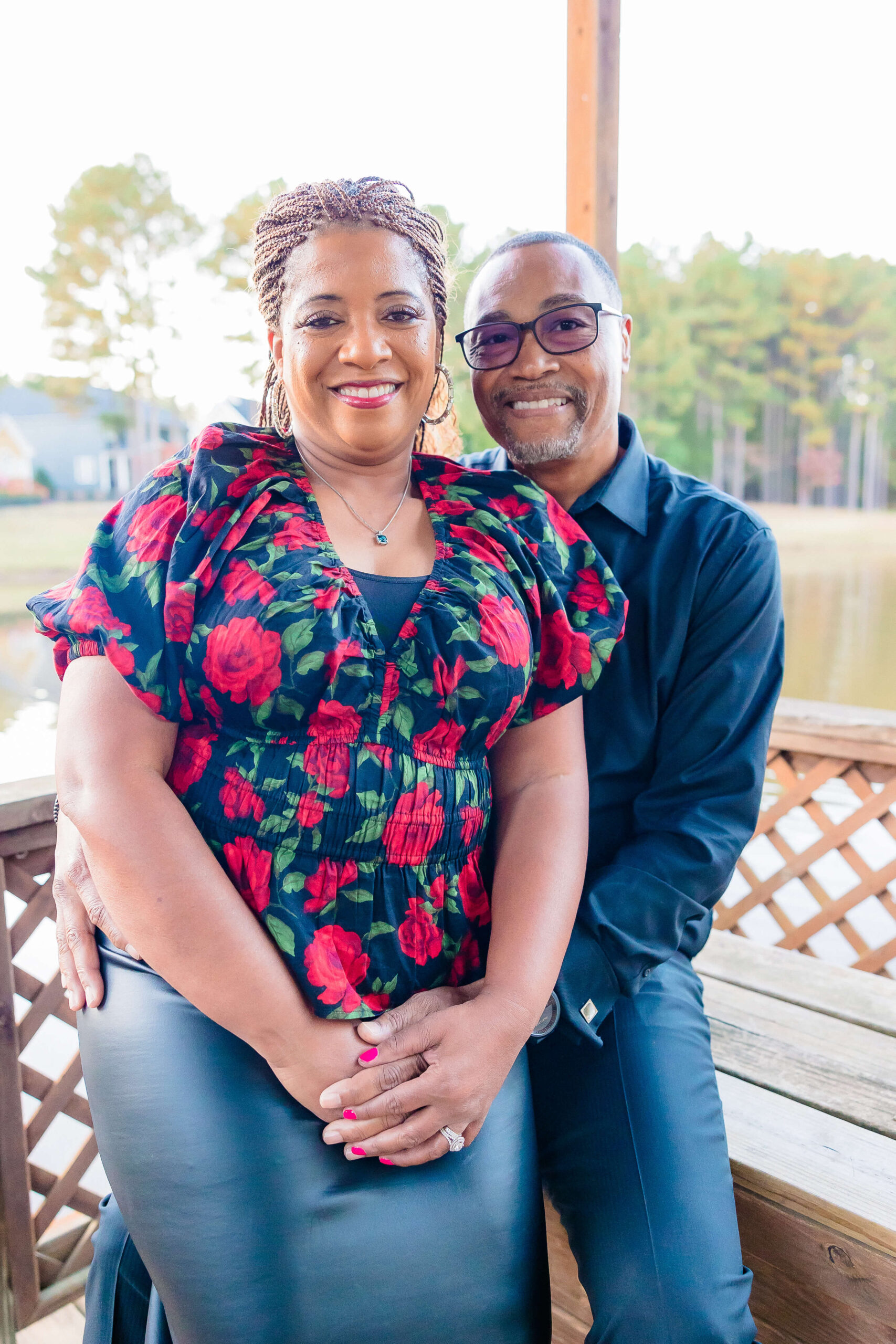 A couple is sitting on a wooden deck bench in a floral blouse and dark shirt.