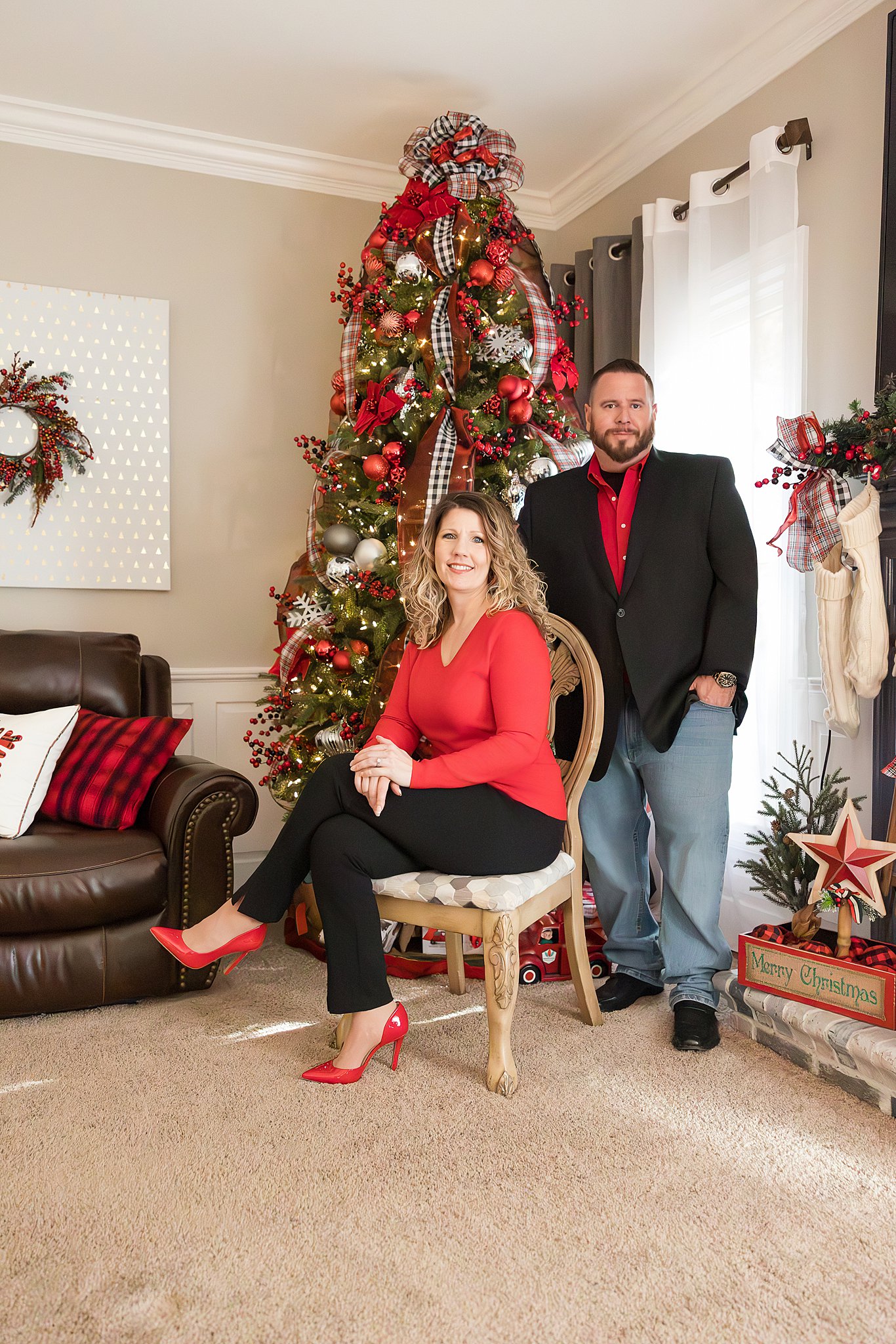 A happy couple sit and stand together in a christmas themed living room in red shirts after visiting hair salons in Fayetteville