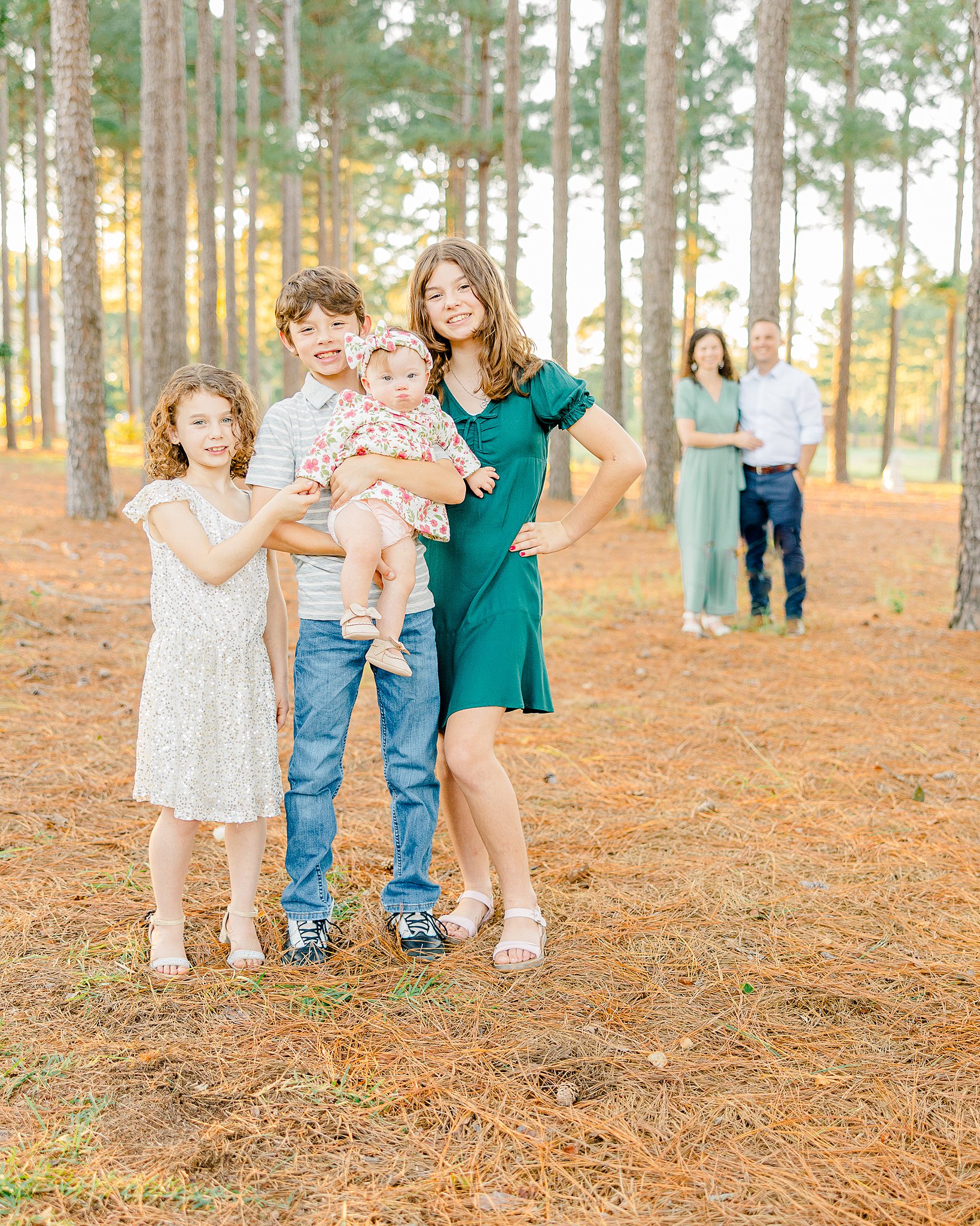 A group of four siblings smile and carry a baby as mom and dad watch from behind them before some Martial Arts Classes For Children In Fayetteville NC