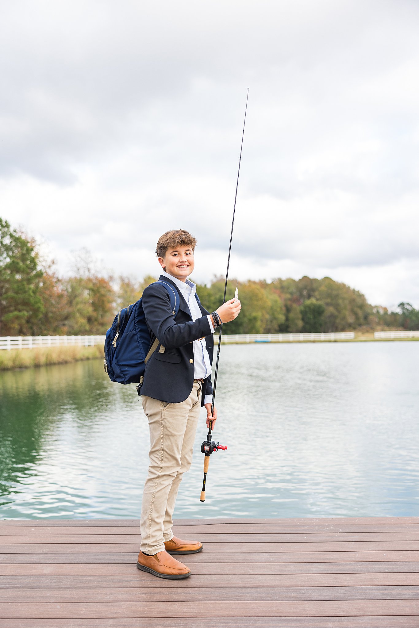 A young teen stands on a wooden dock holding a fishing rod, with a backpack in one of the best parks in fayetteville nc