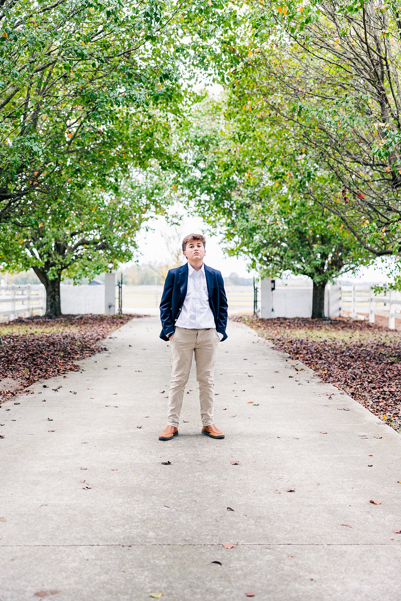 A young boy stands confidently on a tree-lined pathway in a suit in one of the best parks in fayetteville nc