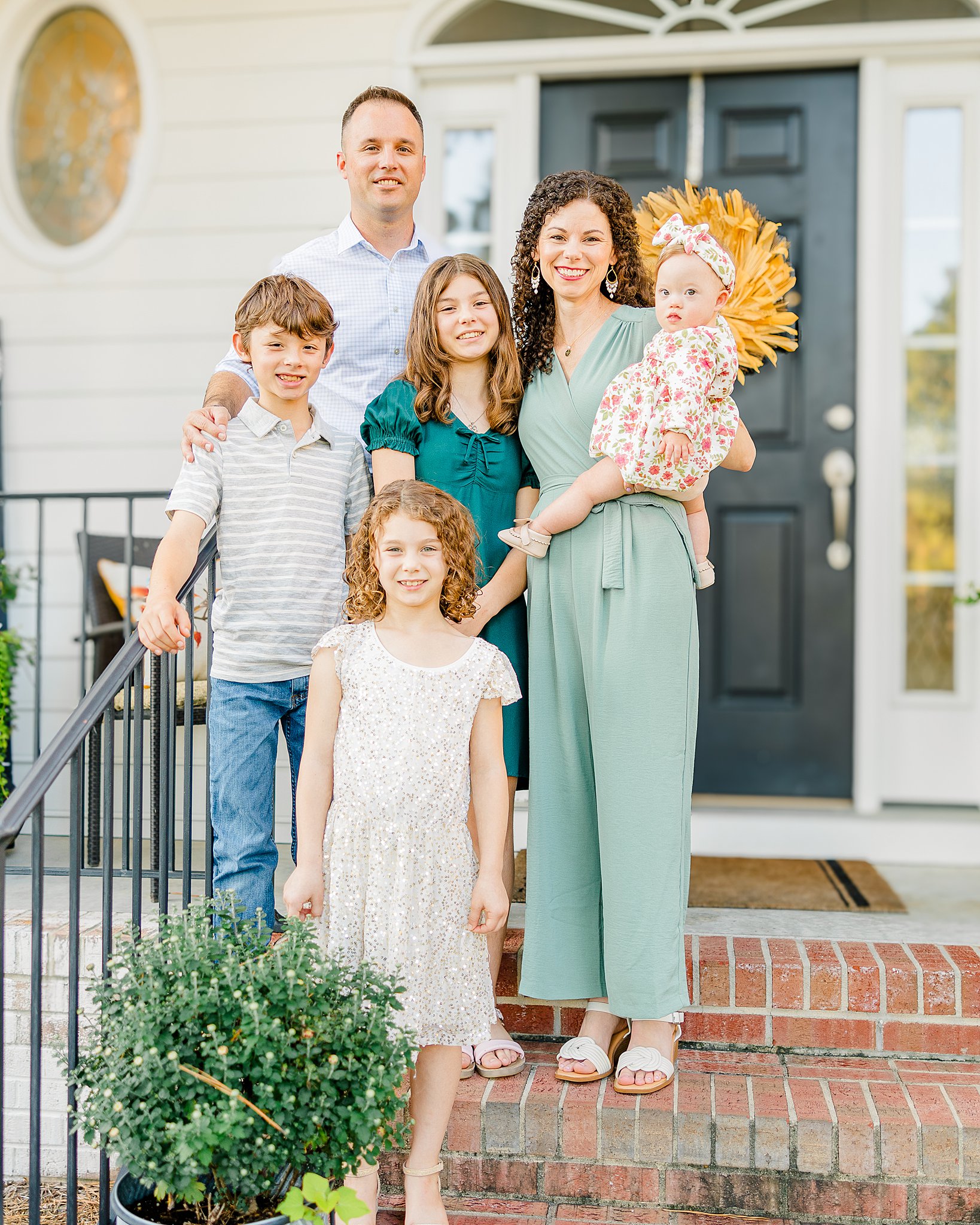 A family of six smiles on the steps in front of a house with a black door before visiting family friendly restaurants fayetteville, nc