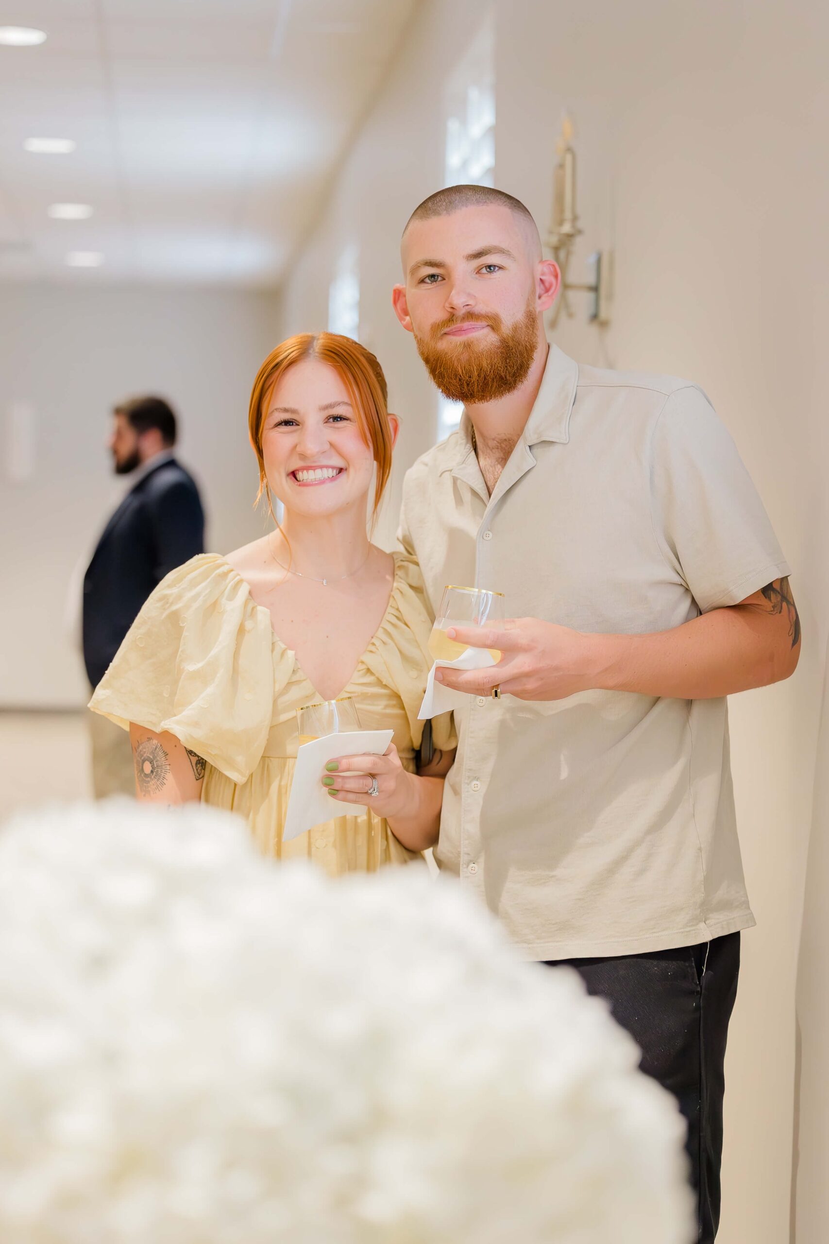 A happy couple in a yellow dress and cream polo stand in a hallway