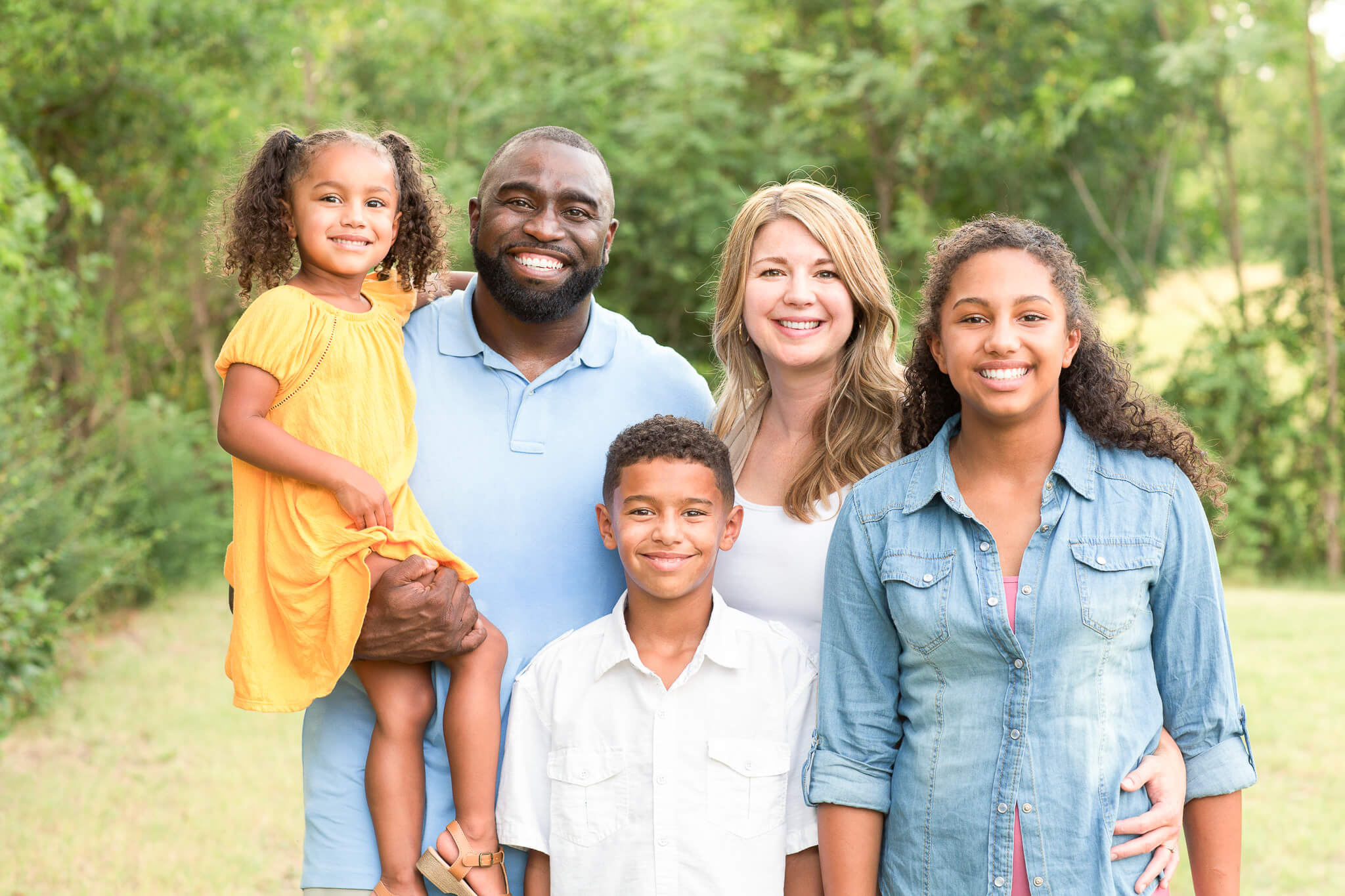 A family of five in a park, smiling with arms around each other