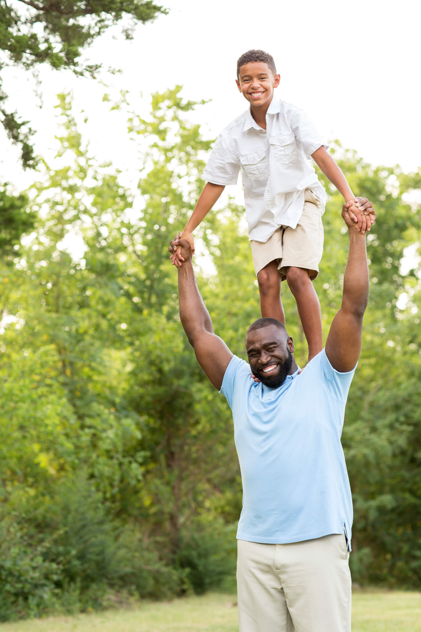 A young boy in a white shirt stands on dad's shoulders in a park after visiting toy stores in Fayetteville, NC