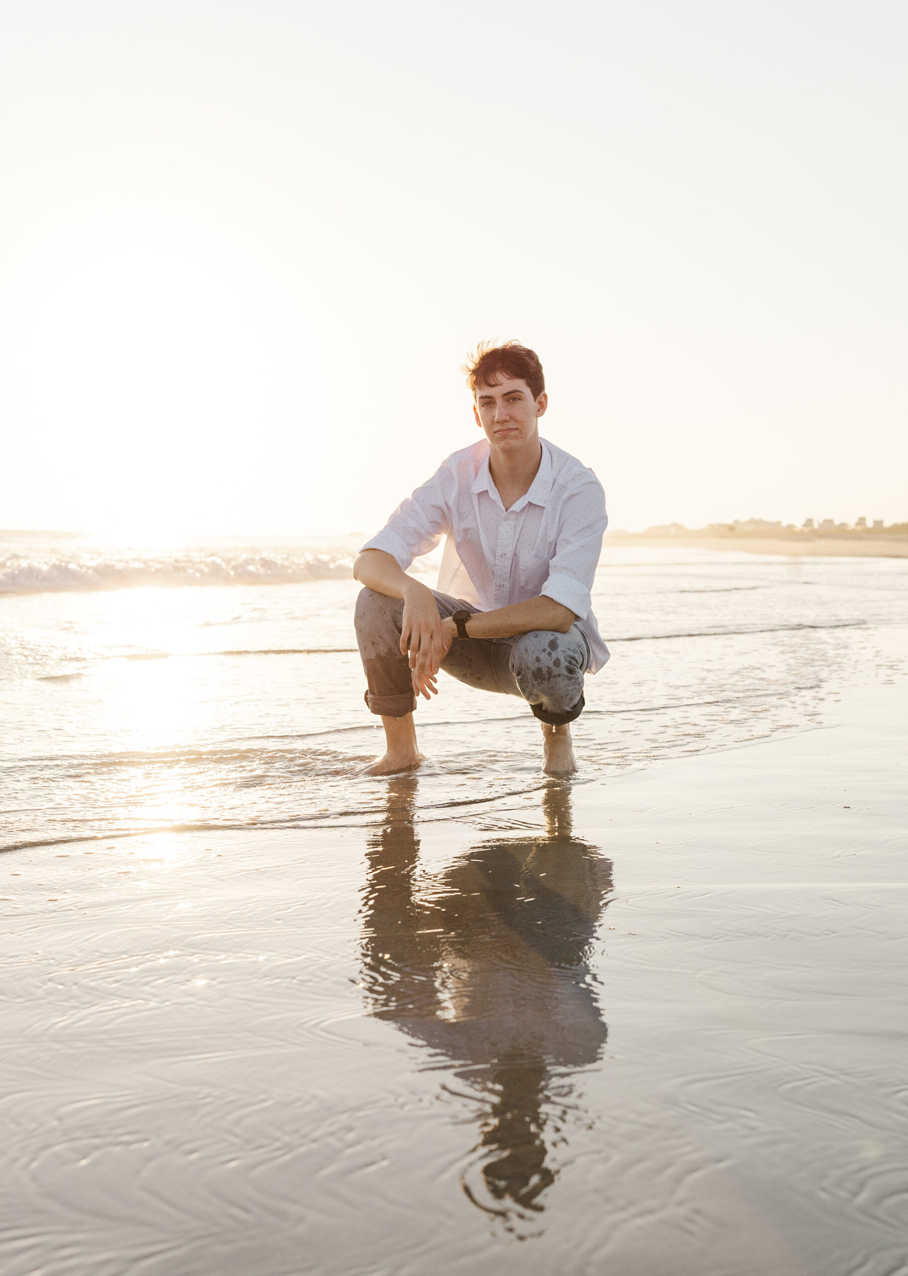 A high school senior in a white shirt and rolled-up pants kneels on a beach after some tutoring in Fayetteville, NC