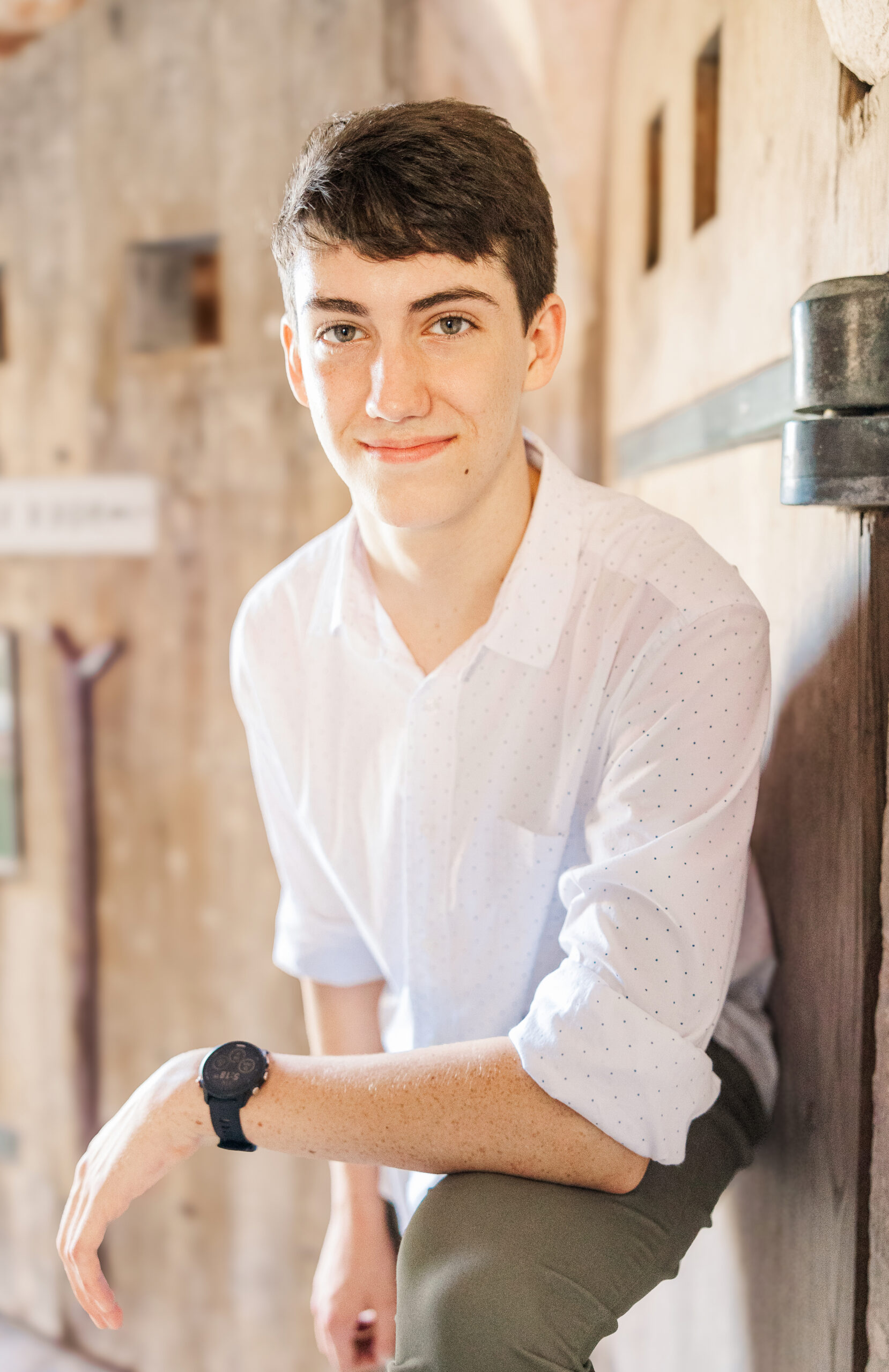 A high school senior in a white shirt leans on his knee outside a stable after some tutoring in Fayetteville, NC