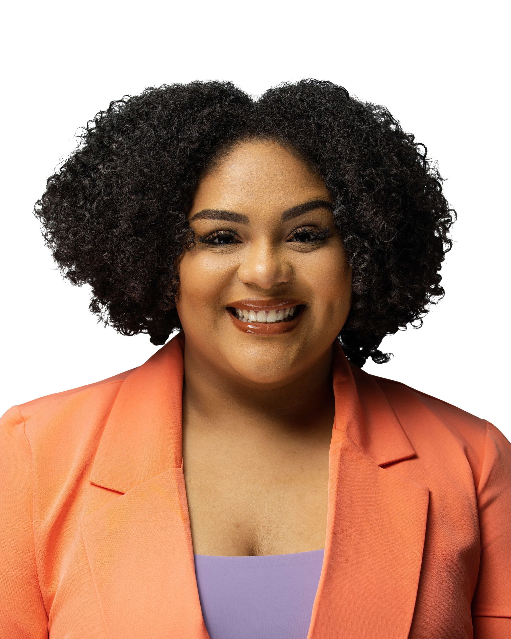 A woman with curly black hair smiles at the camera. She is wearing a coral blazer over a light purple top. The background is plain white. professional headshot photographer Fayetteville NC